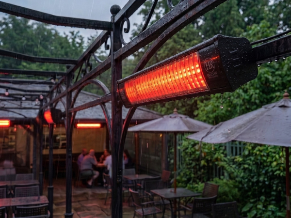Yağmurlu havada klasik bir kafe terasına monte edilmiş, IP55 su korumalı aktif ELCON EIR-2000 ekonomik elektrikli infrared ısıtıcı.